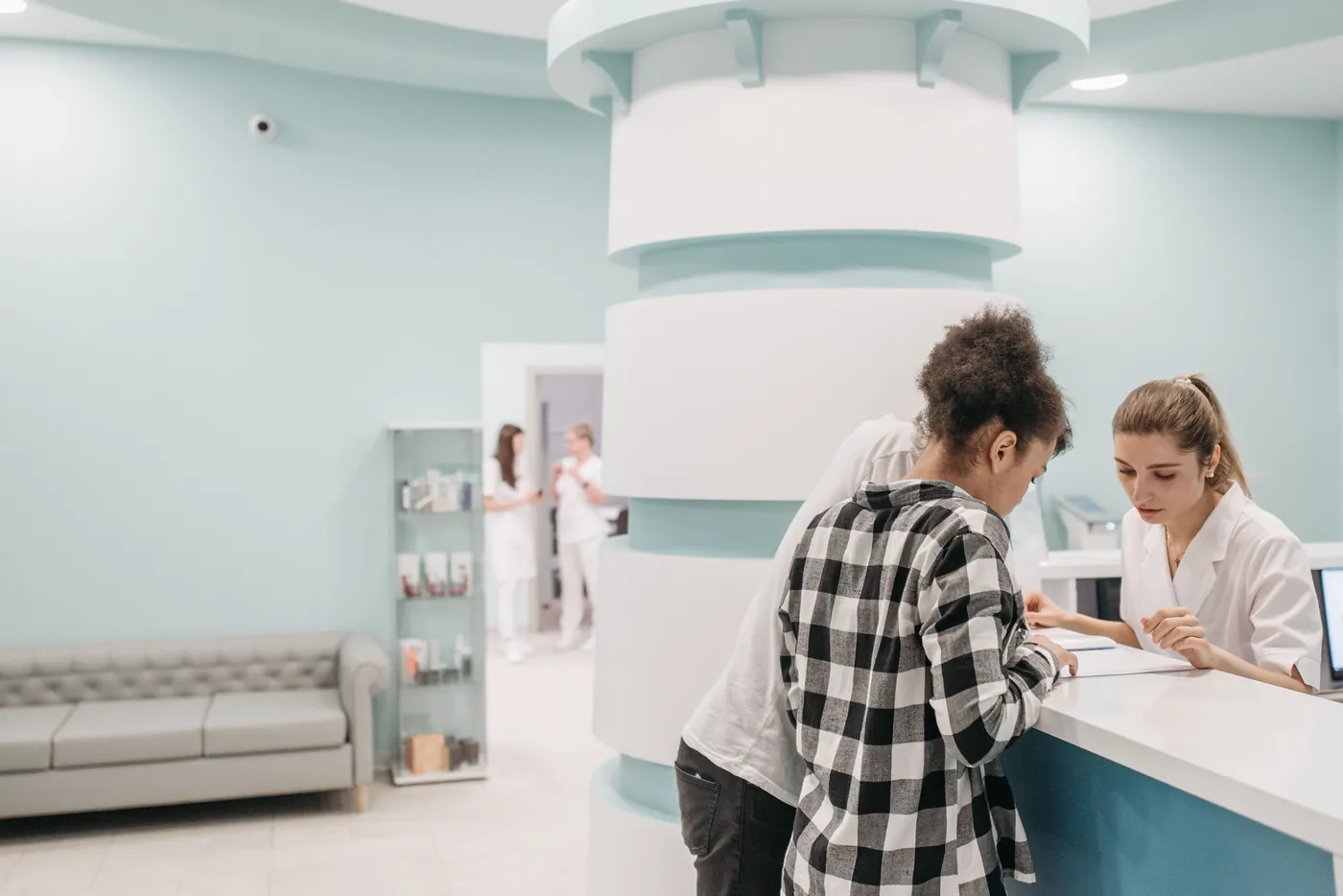 Patient checking in at the reception desk of a small medical office with clinical staff in the background — illustrating the operating environment of a small healthcare practice