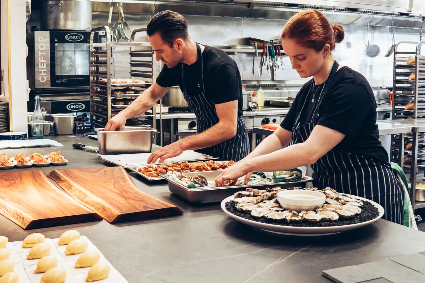 Two restaurant cooks in striped aprons preparing plated dishes in a working kitchen — illustrating the operating environment of a small food service business