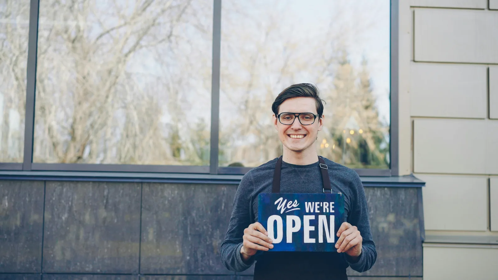 Small business owner holding an open for business sign outside their storefront